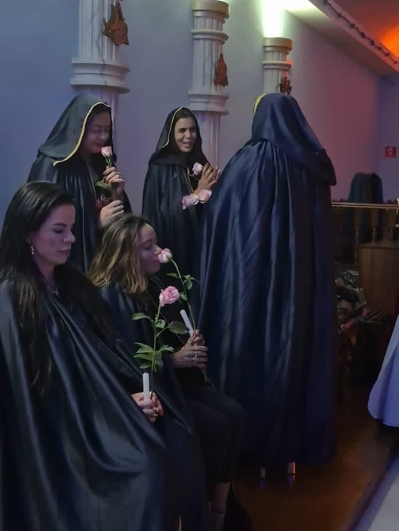 Participantes de capa negra com rosas, em ritual da Ordem